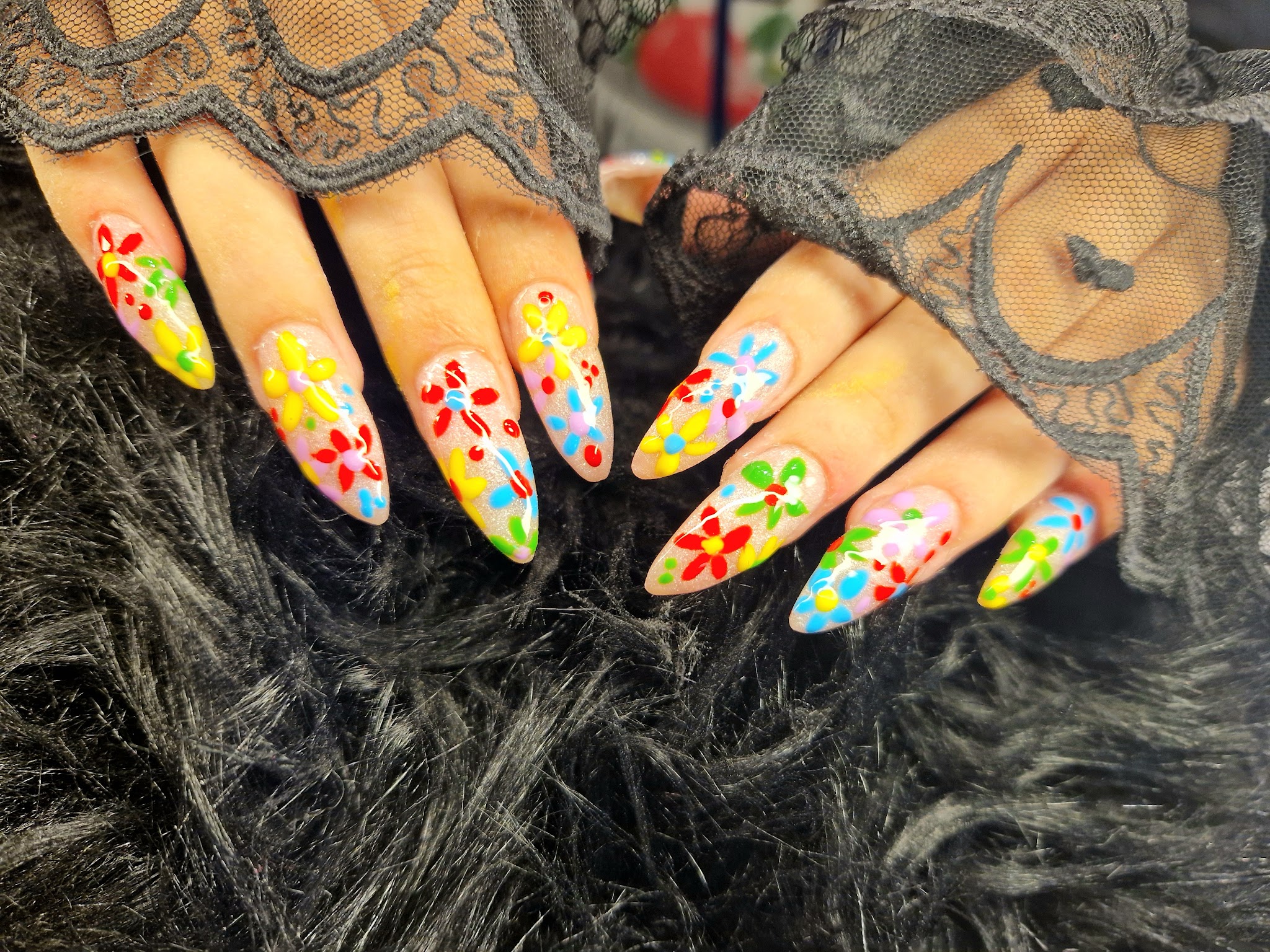 Spitse nagels met kleurrijke bloemetjes in rood, geel, roze en blauw, op zwart kant en bont